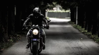 Dynamic Motorcyclist Riding on Dark Tree-Lined Road with Glowing Headlight image