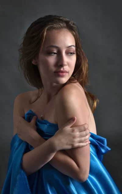 Pensive Young Woman Holding Shimmering Blue Fabric in Elegant Pose image