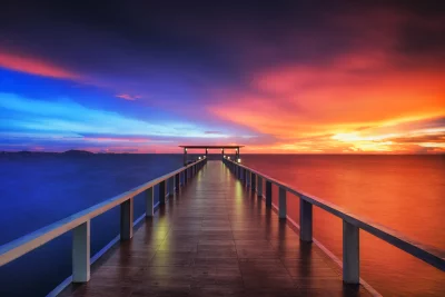 Long Wooden Pier Stretching Towards Horizon with Vibrant Ocean Sunset Cinematic Wallpaper image