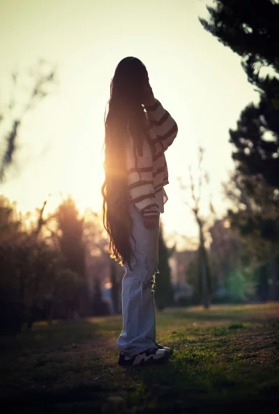 Young Woman with Long Hair Backlit by Golden Sunset in a Peaceful Park