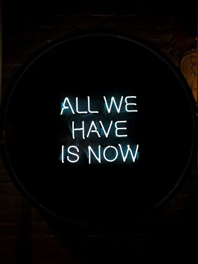 Glowing 'All We Have Is Now' Neon Sign Illuminating a Dark Brick Wall image