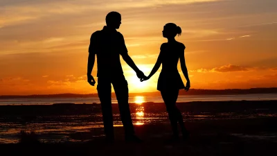 Romantic Couple Holding Hands Against a Vibrant Sunset Over Water image