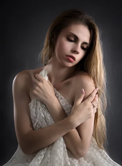 Pensive Young Woman Draped in White Lace Fabric on Dark Background image