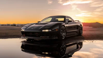 Sleek Black Sports Car Reflecting Golden Sunset Glow in Puddle on Asphalt image