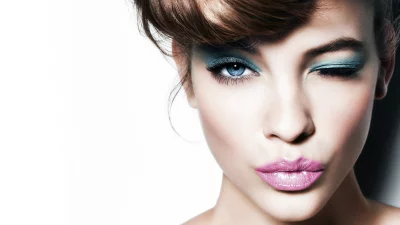 Beautiful Woman with Vibrant Blue Eyeshadow and Pink Glossy Lips Winking Playfully image