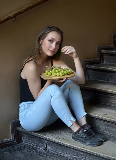 Smiling Young Woman Eating Fresh Grapes on Rustic Wooden Stairs image