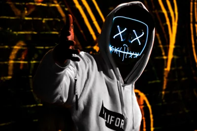 Mysterious Hooded Figure in Glowing Neon Mask Pointing Forward Cinematic Wallpaper image