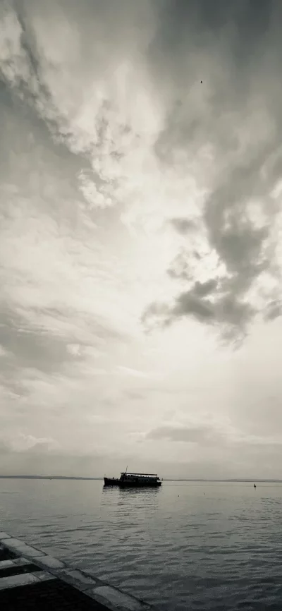 Serene Boat Journey on Expansive Water Under Dramatic Overcast Sky image