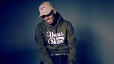 Chris Brown Smiling in Olive Green Hoodie and Beige Cap image