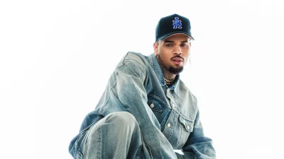 Chris Brown in Denim Jacket and LA Cap Posing Intensely on White Background image
