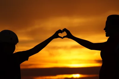 Silhouettes of Mother and Child Forming Heart Hands at Golden Sunset image