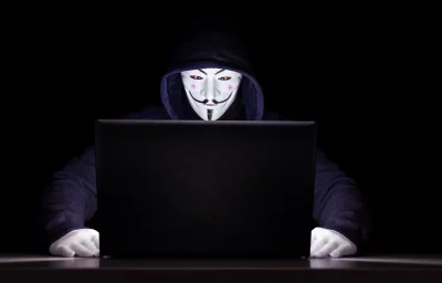 Mysterious Hacker in Anonymous Mask Utilizing Laptop in Darkness image