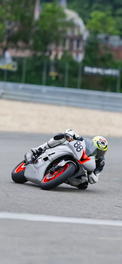 Motorcyclist leans into a tight turn on a sunny racetrack, reaching maximum lean angle.