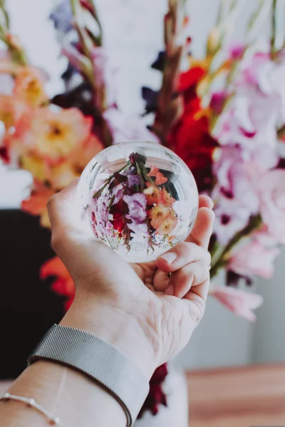 A hand holding a glass ball with flowers inside it