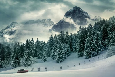 Vintage Red Car Driving Through Snowy Forest Road with Majestic Mountain Peaks image