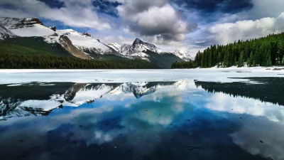 Dramatic winter landscape: snow-capped mountains mirrored in partially frozen alpine lake image