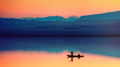 Vibrant Sunset Reflection: Boat with Silhouetted Figures on Calm Lake Against Mountains image