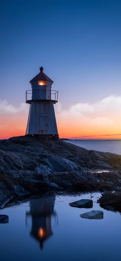 Majestic Lighthouse on Rocky Coast Reflecting in Calm Water at Twilight image
