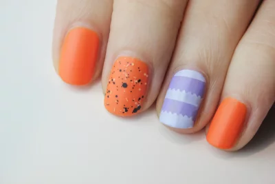 A close-up of a hand with an orange and purple nail polish design