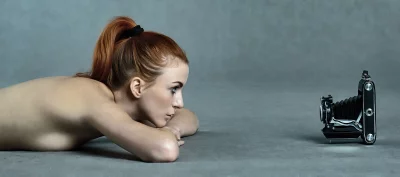 Red-haired Woman Engaged with Vintage Folding Camera on Gray Studio Floor image
