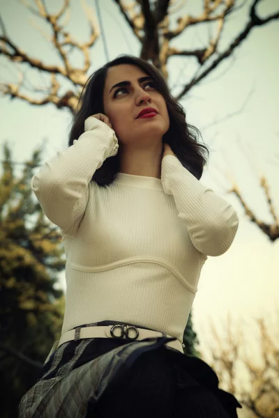 Stylish Woman in White Ribbed Top & Plaid Skirt Contemplatively Looks Up Amidst Autumn Trees