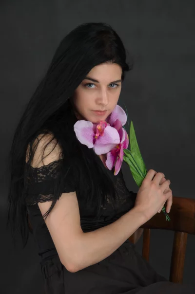 Pensive Young Woman with Long Dark Hair Holding Pink Orchid Flowers image