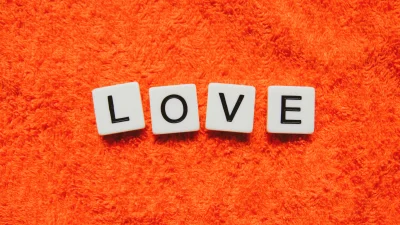 White Game Tiles Spelling 'LOVE' on a Vibrant Orange Fuzzy Textile Background image