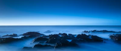 Mystical Blue Ocean Waves Caressing Dark Coastal Rocks at Twilight image