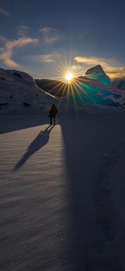 Lone hiker walks towards sunburst in snowy glacial landscape