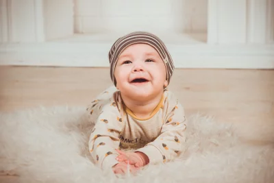 Happy Baby Smiling on Fluffy Rug in Striped Beanie image