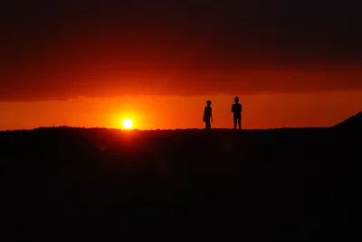 Silhouettes of people standing on a hilltop admiring a vibrant orange sunset image