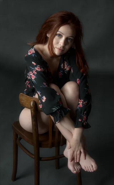 Young Redhead Woman Posing Elegantly in Floral Top on Wooden Chair image