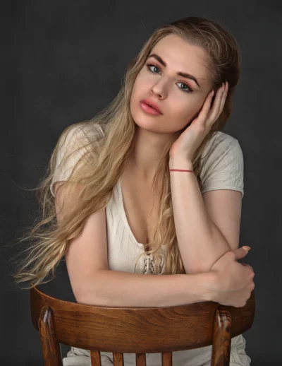 Elegant Blonde Woman Posing Thoughtfully on Wooden Chair image