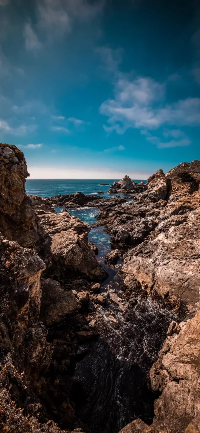 Rugged Coastal Rocks with Ocean Waves Under a Bright Blue Sky