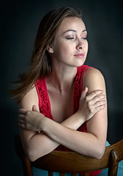 Pensive Young Woman with Crossed Arms in Red Top on Wooden Chair image
