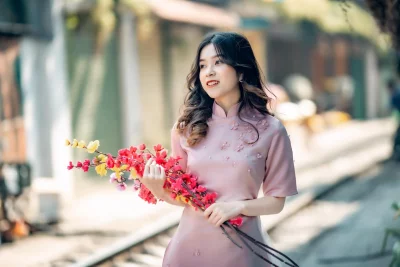 A young woman model in a pink dress standing in a park, surrounded by trees and flowers
