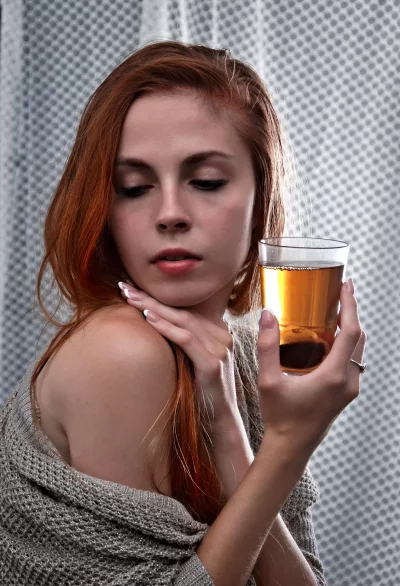 Elegant Red-Haired Woman Holding Amber Beverage in Contemplative Pose image
