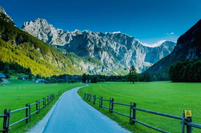 Scenic Mountain Road Winding Through Lush Green Valley with Towering Peaks and Clear Sky image