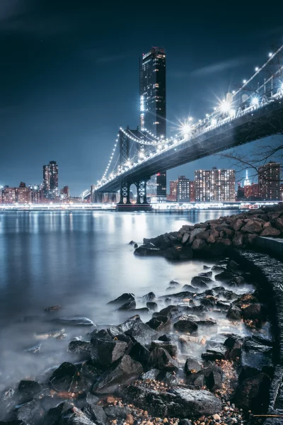 Iconic Manhattan Bridge Nightscape with NYC Skyline, Motion Blur Water, and Rocky Foreground image