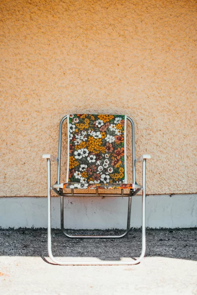 a vintage floral pattern lawn chair sitting at an angle in front of a yellow wall