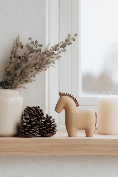 Wooden horse toy, pinecones, and candle on a shelf