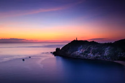 Vibrant Coastal Sunset with Lighthouse and Serene Ocean View image