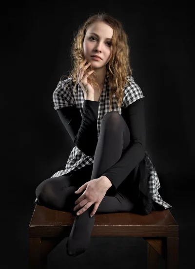 Pensive Young Woman with Curly Hair and Checkered Blouse on Dark Background image