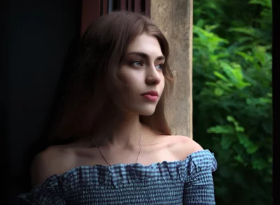Pensive Young Woman Gazing Outdoors from Window with Lush Green View image