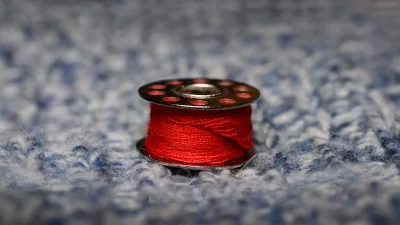 Vibrant Red Sewing Thread Bobbin on Blue Knitted Background image