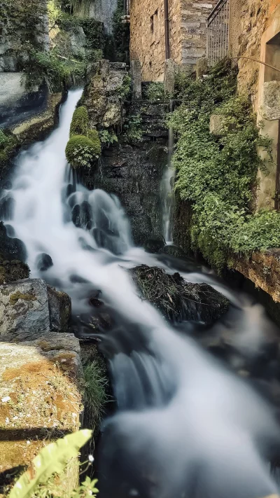 Silky smooth waterfall cascading over mossy rocks and stone buildings
