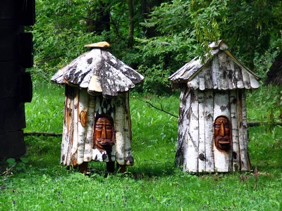 Handcrafted Birch Bark Beehives with Unique Carved Faces in Lush Green Forest image