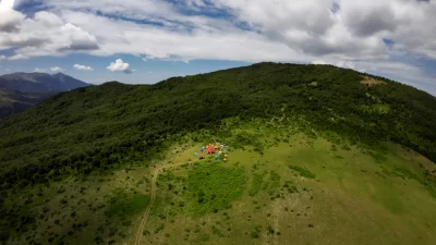 Aerial view of a campsite with colorful tents on a lush green mountainside under a cloudy sky