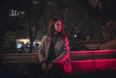 Woman in Coat Sitting Outdoors at Night with Red Light Accent