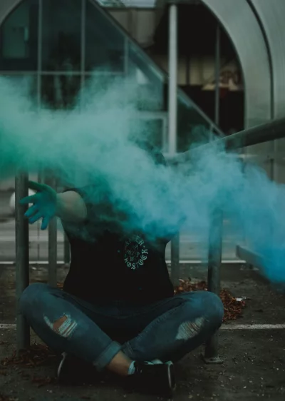 A woman sits on the ground with her hand outstretched, and green smoke billows out from behind her